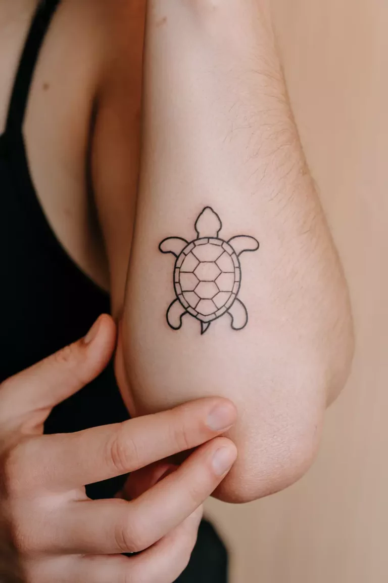 A close-up photo of a woman showing her tiny minimalist turtle outline tattoo design  on her arm