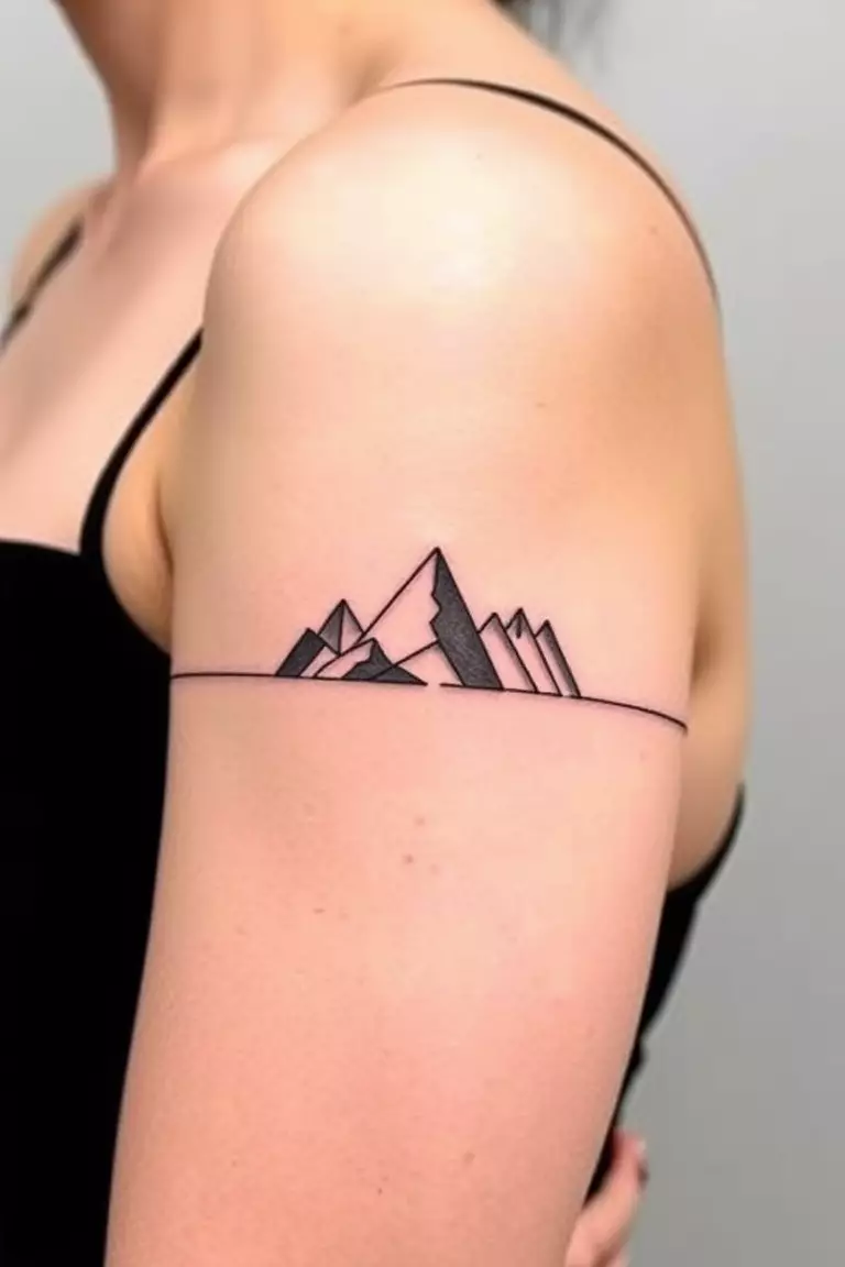 Mountain Armband Tattoo A photo of a woman with a mountain armband tattoo encircling her bicep, featuring stylized peaks and valleys.