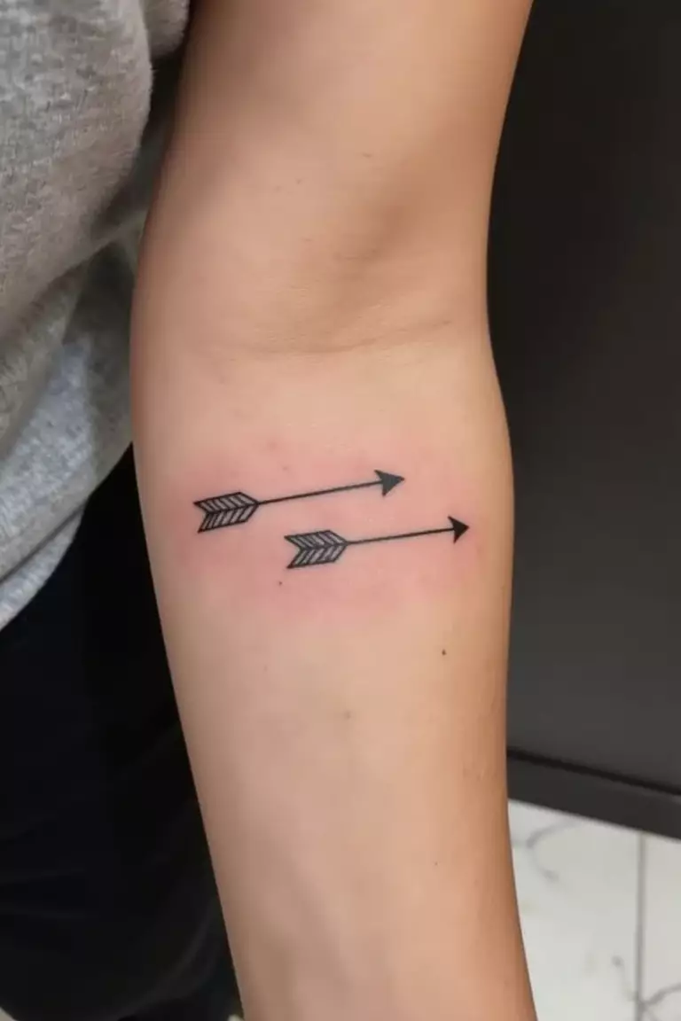 Double Arrow Tattoo A close up shot of woman's arm with a black ink double arrow tattoo, parallel arrows pointing in opposite directions