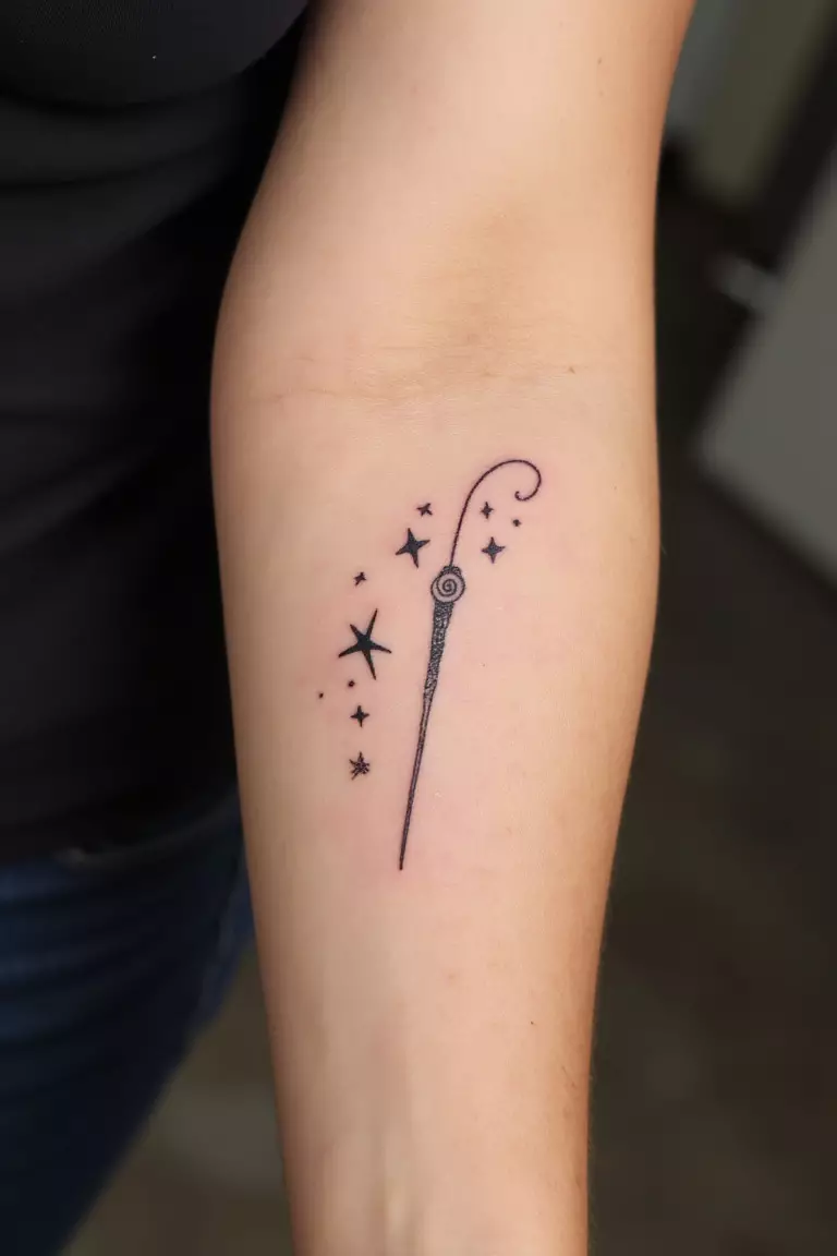 Wand Tattoo A close up shot of woman's arm with a black ink tattoo of a delicate wand with surrounding stars.