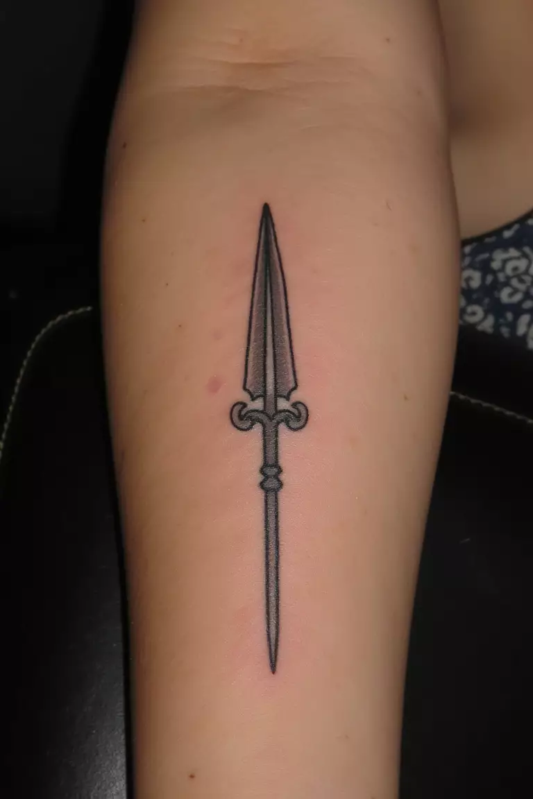Ares's Spear A close up shot of woman's arm with a black ink tattoo of a small spear representing Ares.
