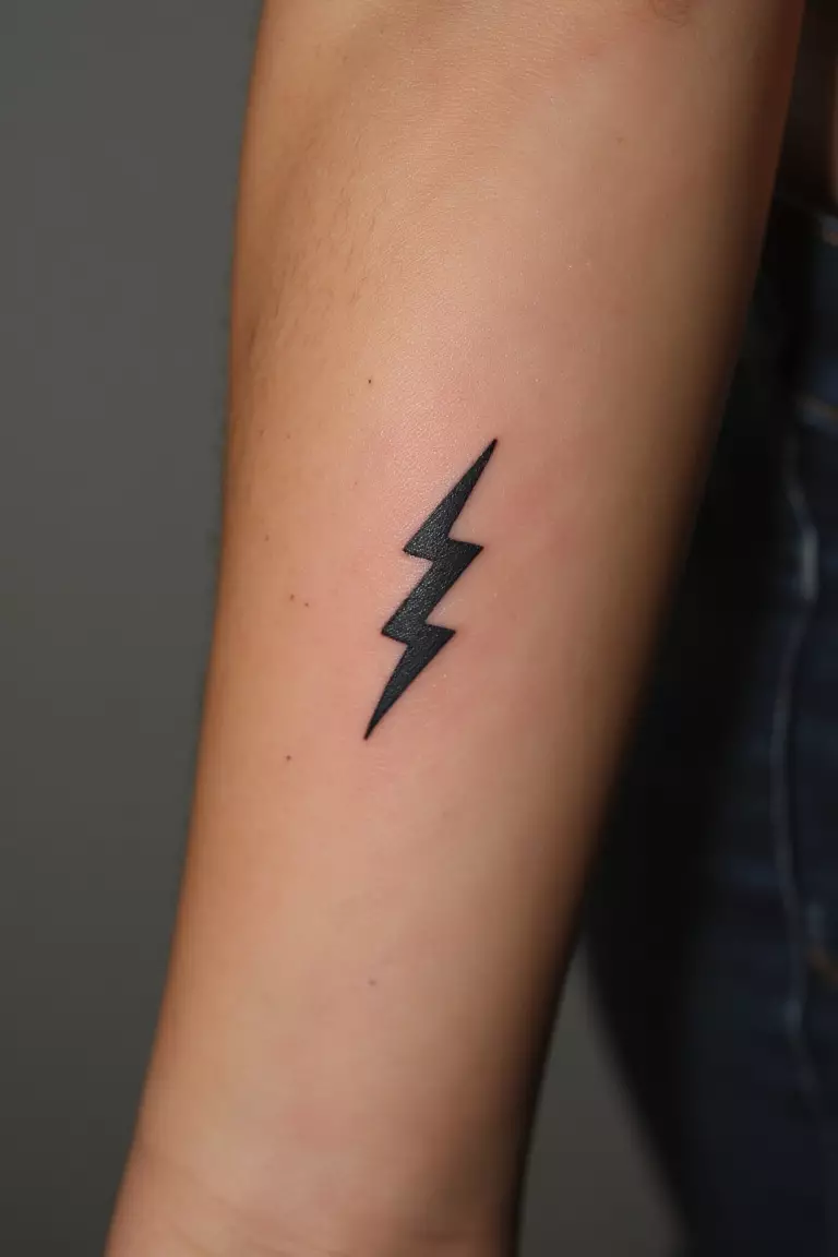 Zeus's Lightning Bolt A close up shot of woman's arm with a black ink tattoo featuring a small, stylized lightning bolt symbolizing Zeus's power and authority.
