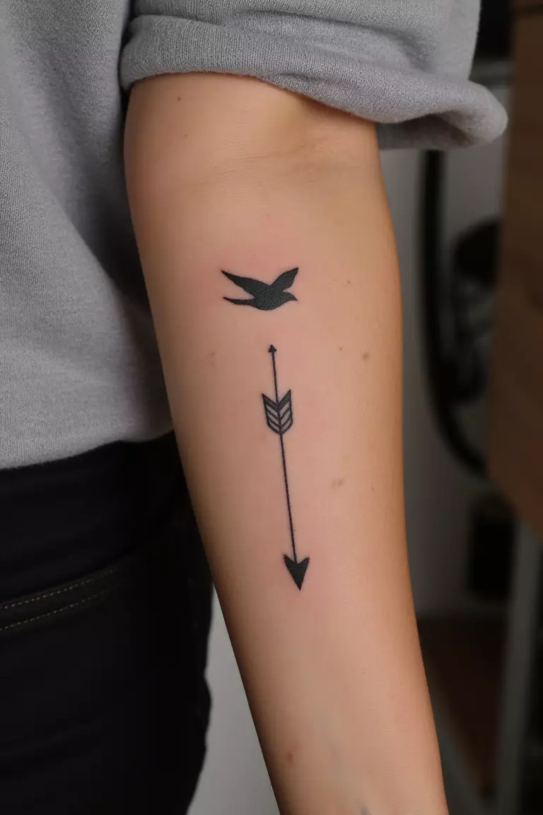 Arrow and Bird Tattoo A close up shot of woman's arm with a black ink arrow and bird tattoo, bird flying near the arrow