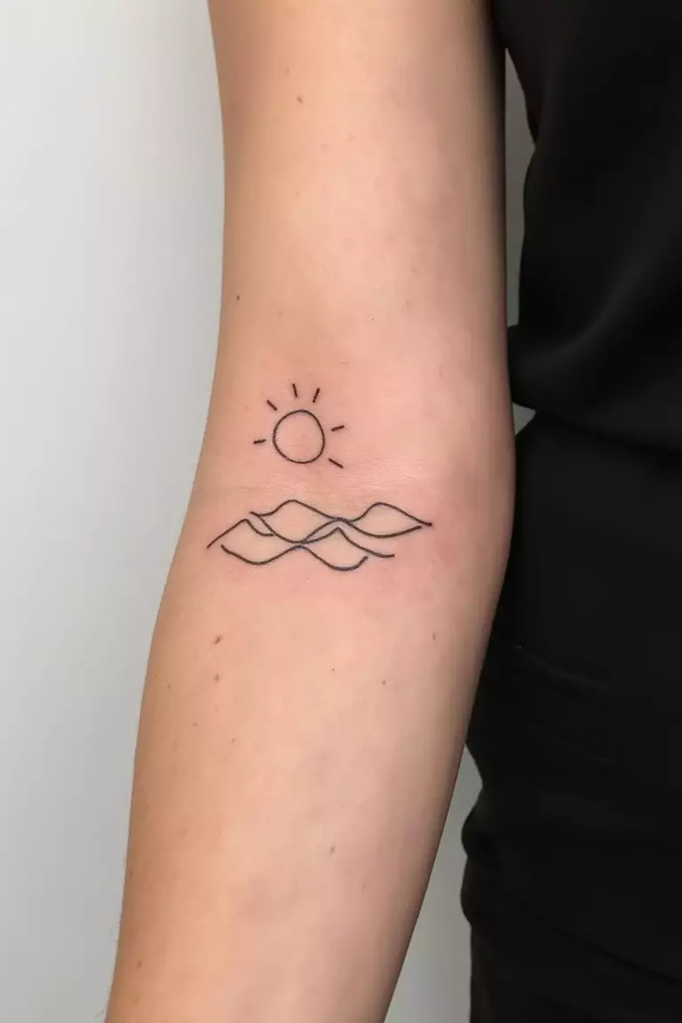 Little Sea A close up shot of woman's arm with a black ink tattoo featuring minimal wave lines with a small outline of sun, perfect summer-themed design.