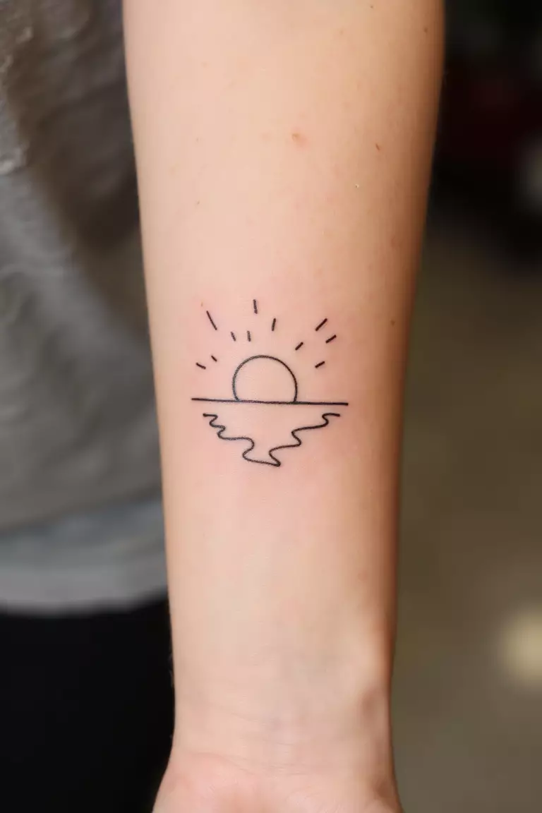 Sunrise & Sunsets A close up shot of woman's arm with a black ink tattoo showing a minimal line outline of a sun setting over reflected water, tranquil beach-inspired design.