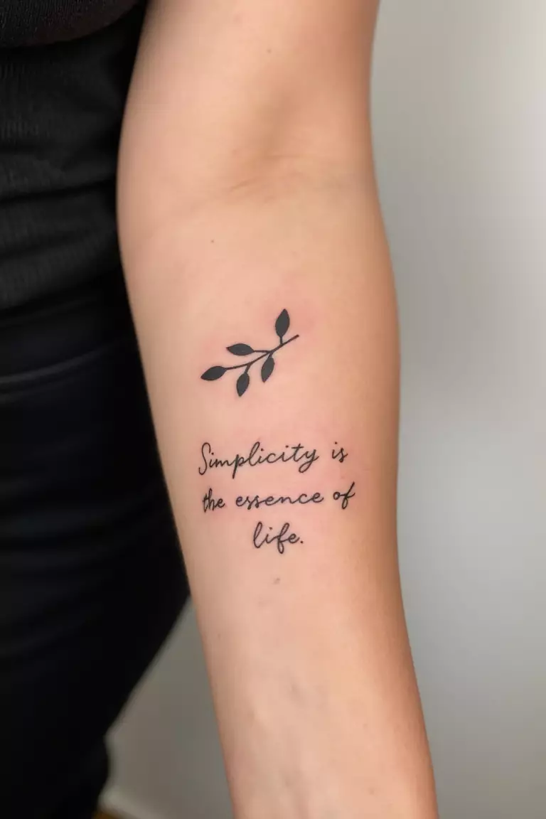 Olive Branch With A Minimalist Quote A close up shot of woman's arm with a black ink olive branch accompanied by a minimalist quote "Simplicity is the essence of life" tattoo
