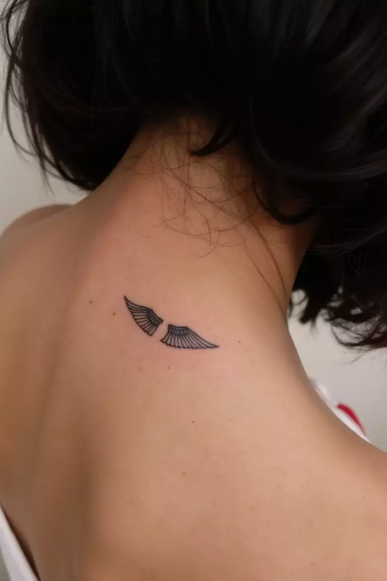 Tiny Wings Tattoo A close up shot of woman's neck from the back with a black ink tiny wings tattoo
