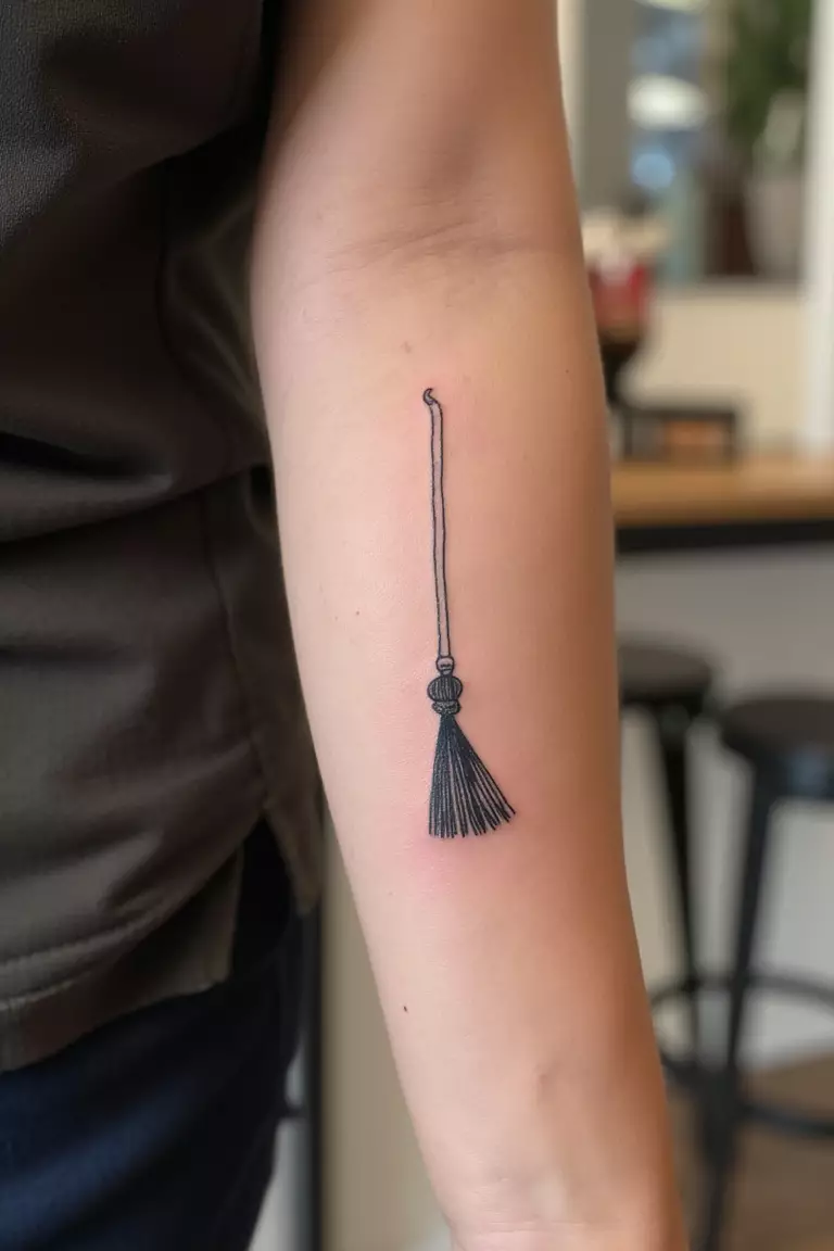 Witch's Broom Tattoo A close up shot of woman's arm with a black ink tattoo of a minimalistic broom.