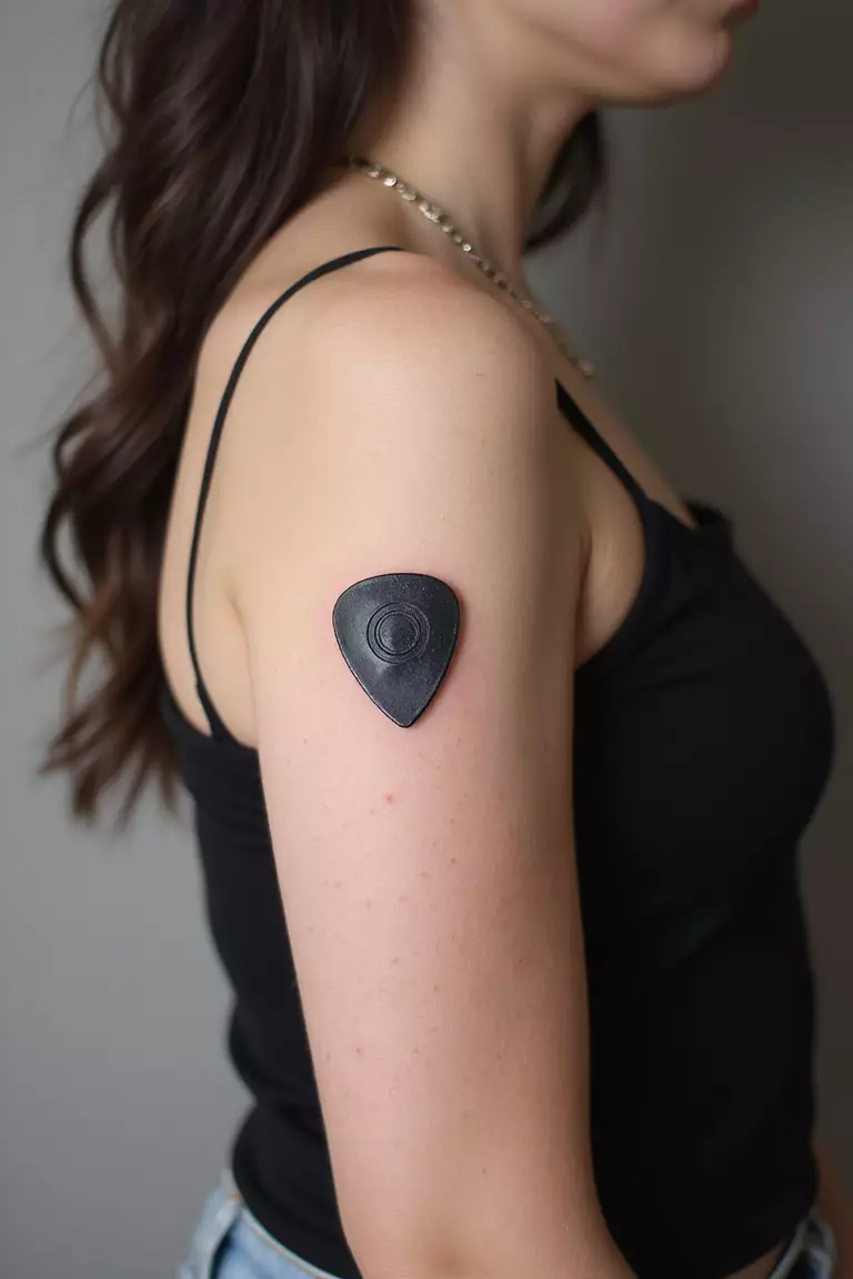 Guitar Pick A close-up shot of a woman showing her black ink single guitar pick tattoo on her arm.