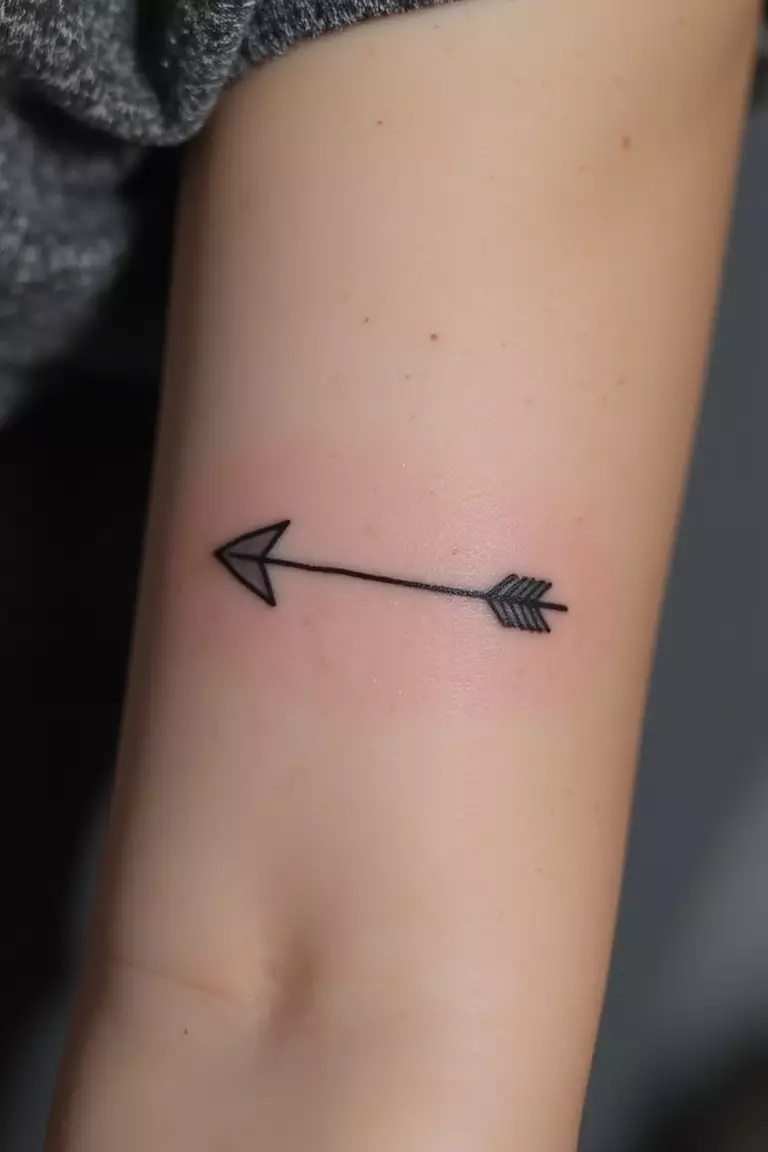 Arrow A close-up shot of a woman's arm with a black ink tattoo of a single arrow pointing forward.