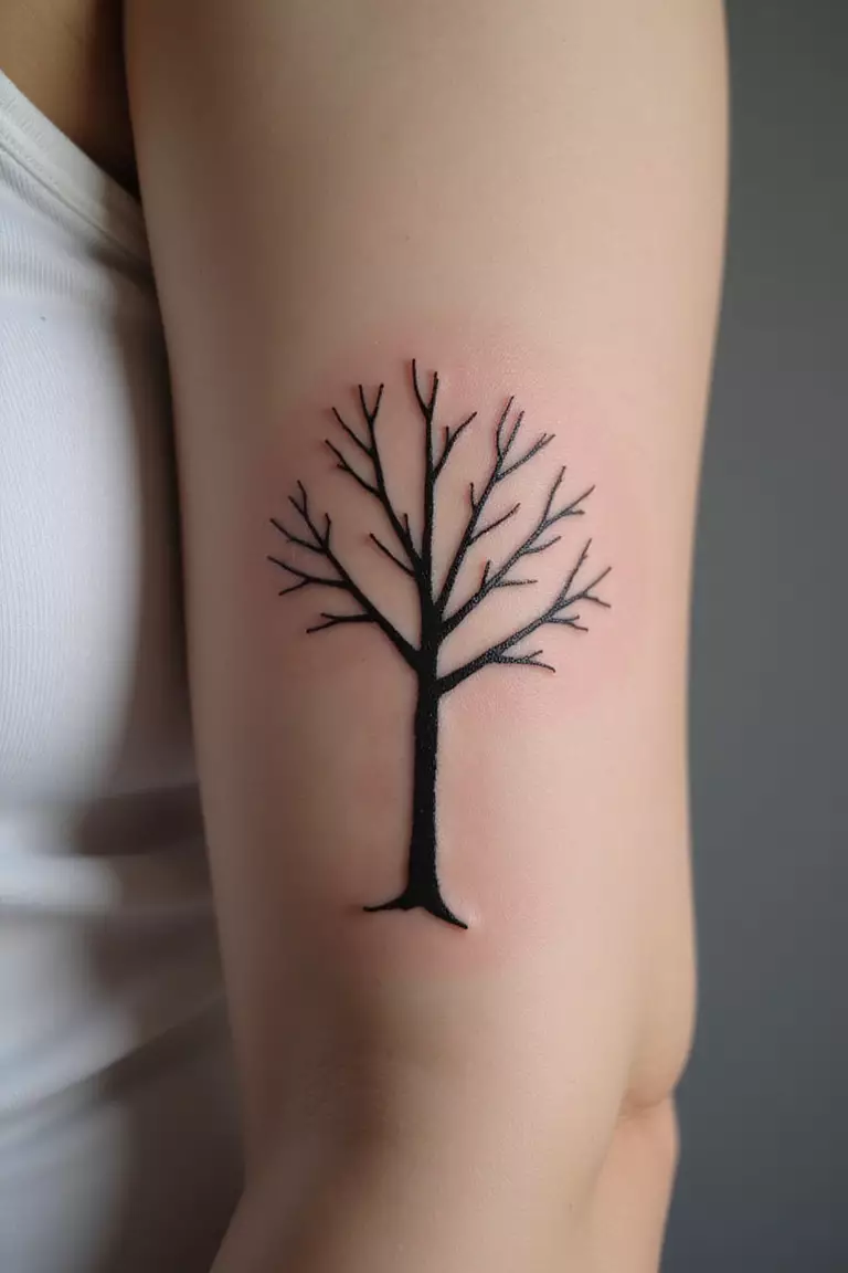 Tree Symbol A close-up shot of a woman's arm with a black ink tattoo of a very simple, almost stick-figure-like tree.