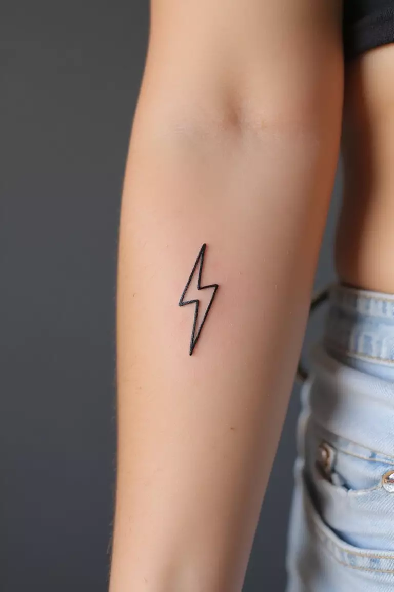 Lightning Bolt A close-up shot of a woman's arm with a black ink tattoo of a tiny, simple lightning bolt outline.