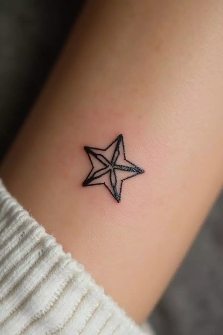 Star Symbol A close-up shot of a woman's arm with a black ink tattoo of a tiny, simple five-pointed star outline.