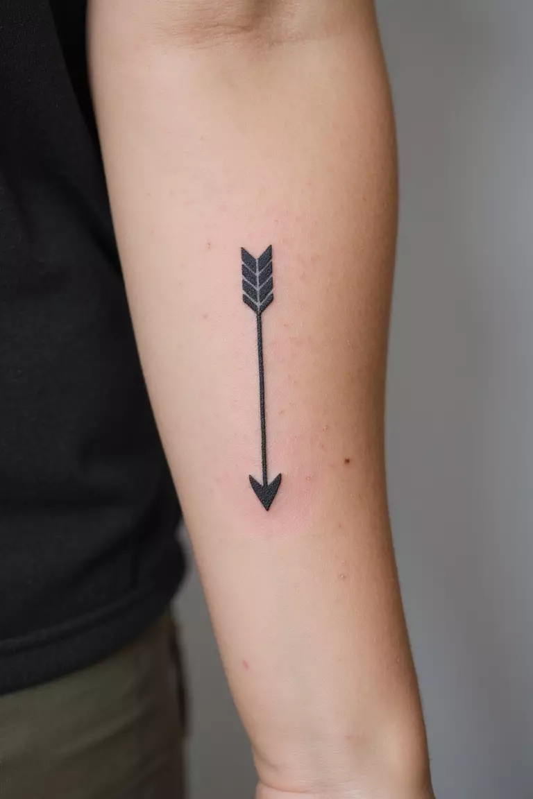 Arrow Design A close-up shot of a woman's arm with a black ink tattoo of a simple, thin black arrow.