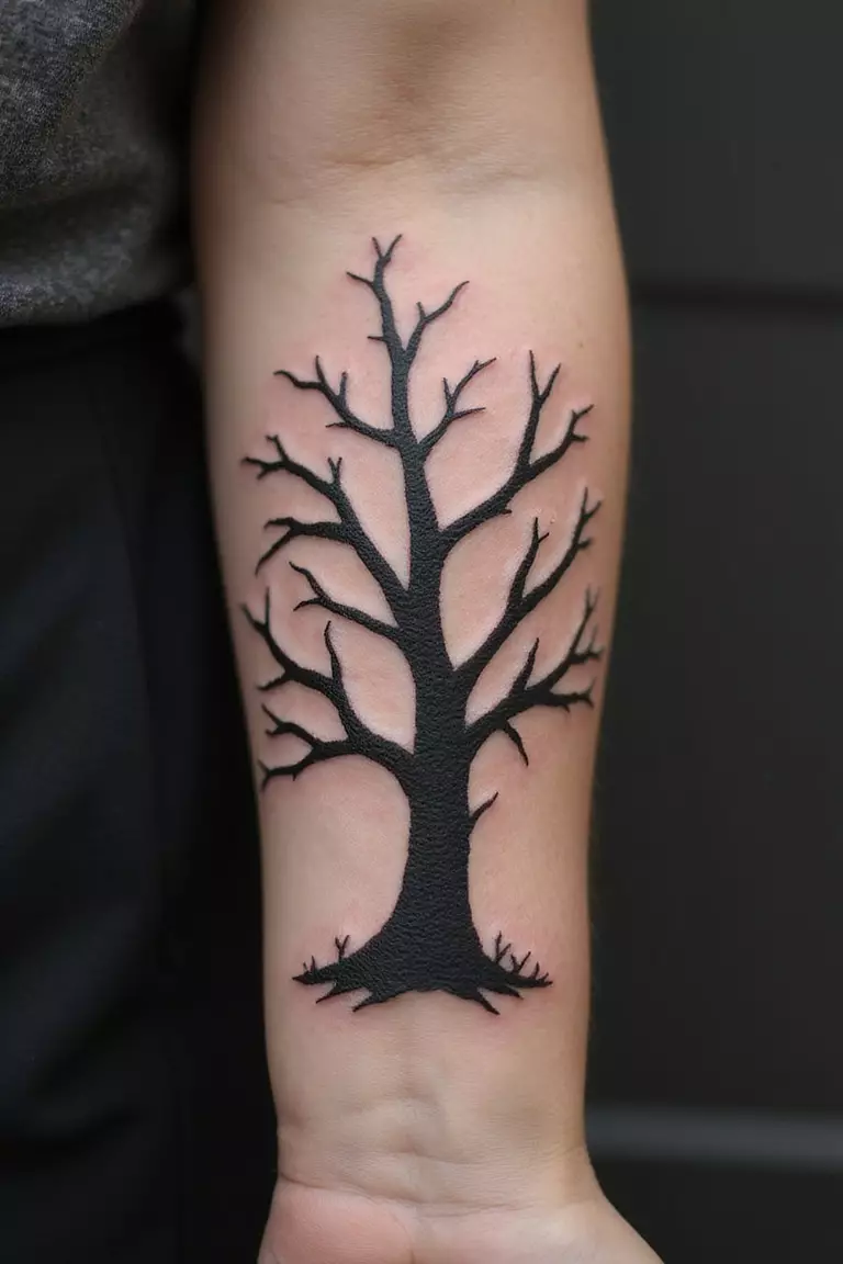 Lifeless Tree A close-up shot of a woman's arm with a black ink tattoo of a lifeless tree.